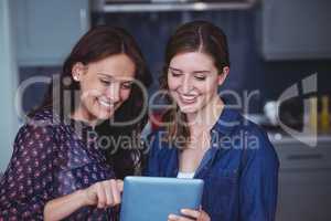 Two beautiful women using digital tablet in kitchen