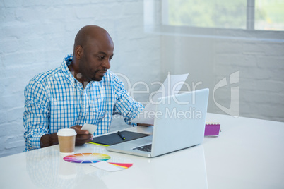 Graphic designer reading a document with laptop on table