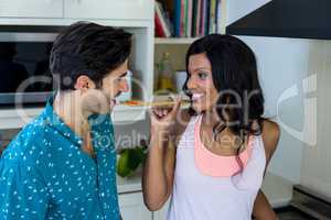 Woman feeding man while cooking in kitchen