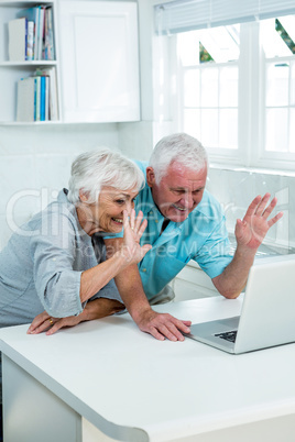 Senior couple waving hands while using laptop