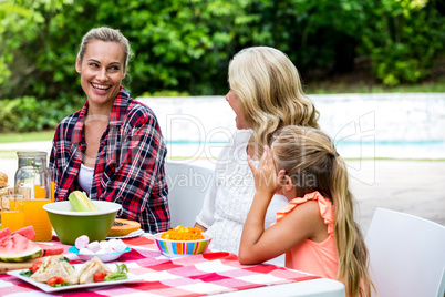 Smiling woman taking to mother and daughter at table