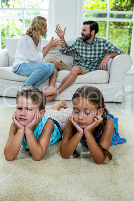 Upset children lying against parents fighting at home