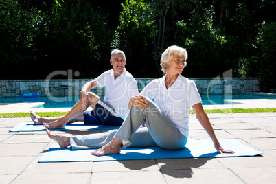 Senior couple exercising on mat at poolside