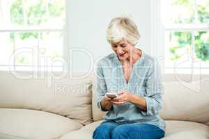 Smiling senior woman using mobile phone on sofa