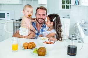 Smiling man with two children having breakfast in kitchen