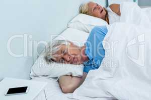 Thoughtful senior man relaxing on bed with phone on table