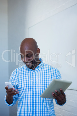 Man text messaging on mobile phone and holding digital tablet