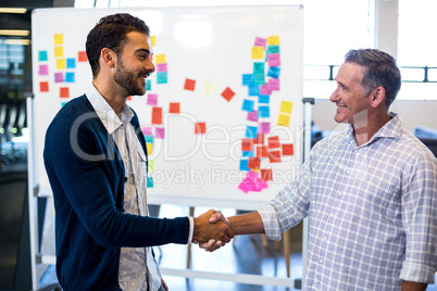 Colleagues shaking hands in front of white board