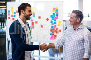 Colleagues shaking hands in front of white board