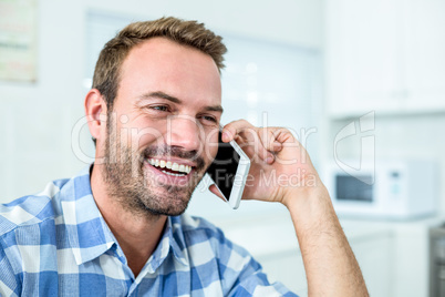 Happy man talking on cellphone while sitting in kitchen