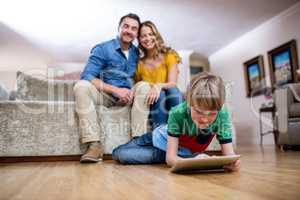 Boy using a digital tablet while parents sitting on sofa in back