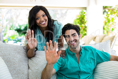 Portrait of young couple sitting on sofa and waving hand