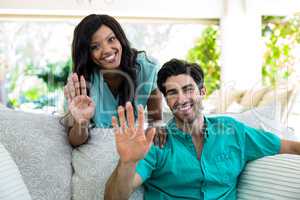 Portrait of young couple sitting on sofa and waving hand