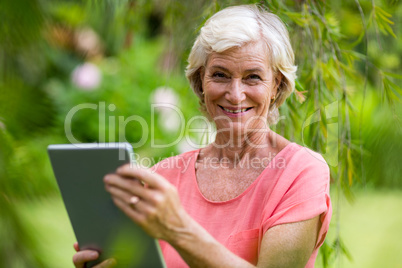 Smiling senior woman holding phone in yard