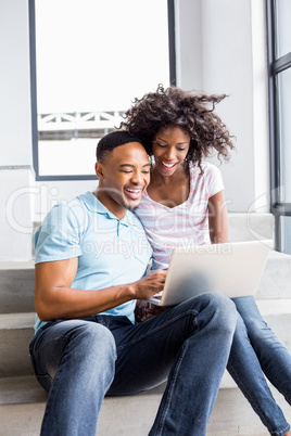 Happy couple sitting on steps and using laptop