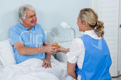 Nurse giving juice to smiling senior man