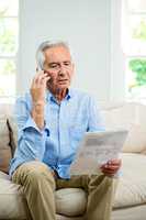 Senior man reading document while talking on phone at home