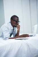 Young man lying on bed and using laptop