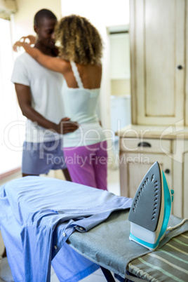 Iron and a shirt on ironing board and couple in background