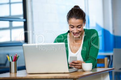 Woman using mobile phone with laptop on table