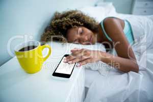 Woman touching her mobile phone while sleeping on bed
