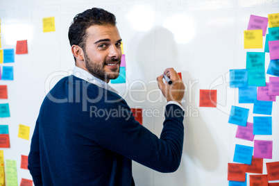 Young man smiling at camera while writing on white board