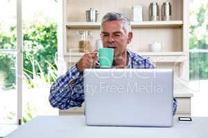 Senior man drinking coffee while using laptop