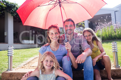 Happy family sitting in garden under a red umbrella