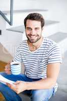 Portrait of happy man on steps holding cup of coffee and reading