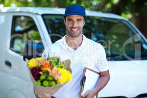 Smiling delivery man holding flower bouquet and clipboard