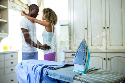 Iron and a shirt on ironing board and couple in background