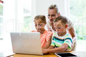 Mother teaching children to use laptop at home