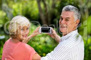 Senior couple taking selfie while standing in yard