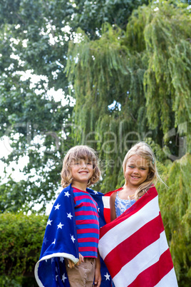 Portrait of siblings wrapped in American flag at back yard