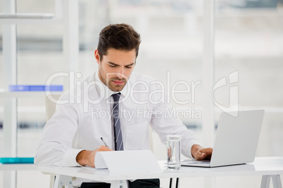 Businessman using laptop and taking notes