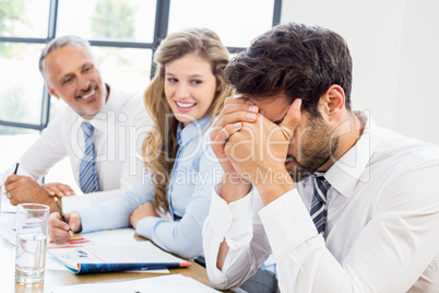 Smiling colleagues looking at frustrated businessman