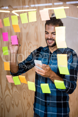 Man using mobile phone while writing on sticky notes