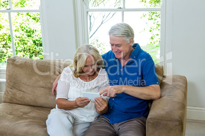 Smiling senior couple using mobile phone while sitting at home