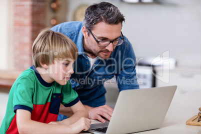 Father and son using laptop in kitchen