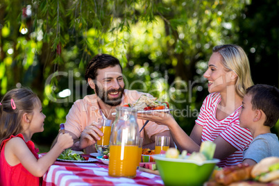 Mother offering salad while family sitting at table