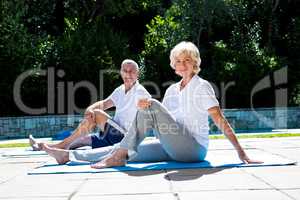 Smiling couple on exercise mat at poolside