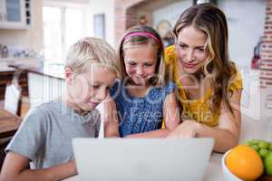 Mother and kids using laptop in kitchen