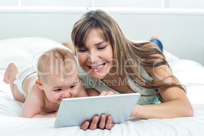 Woman showing digital tablet to son while lying on bed