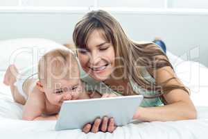 Woman showing digital tablet to son while lying on bed