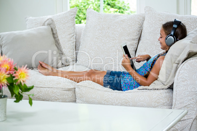 Girl using digital table and listening music while relaxing on s