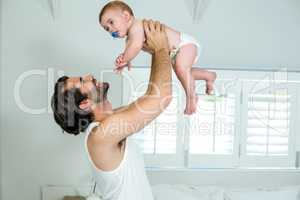 Father playing with son by bed at home