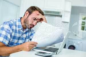 Tensed man looking in documents while sitting by laptop at table