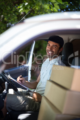 Portrait of happy delivery man writing in clipboard