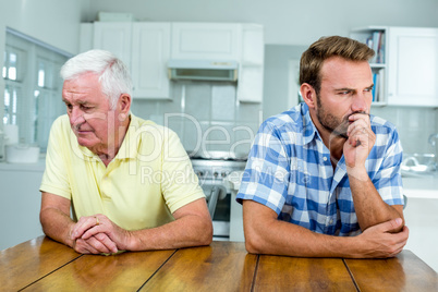 Tensed father and son sitting at table in kitchen