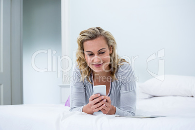 Smiling woman using phone while lying on bed